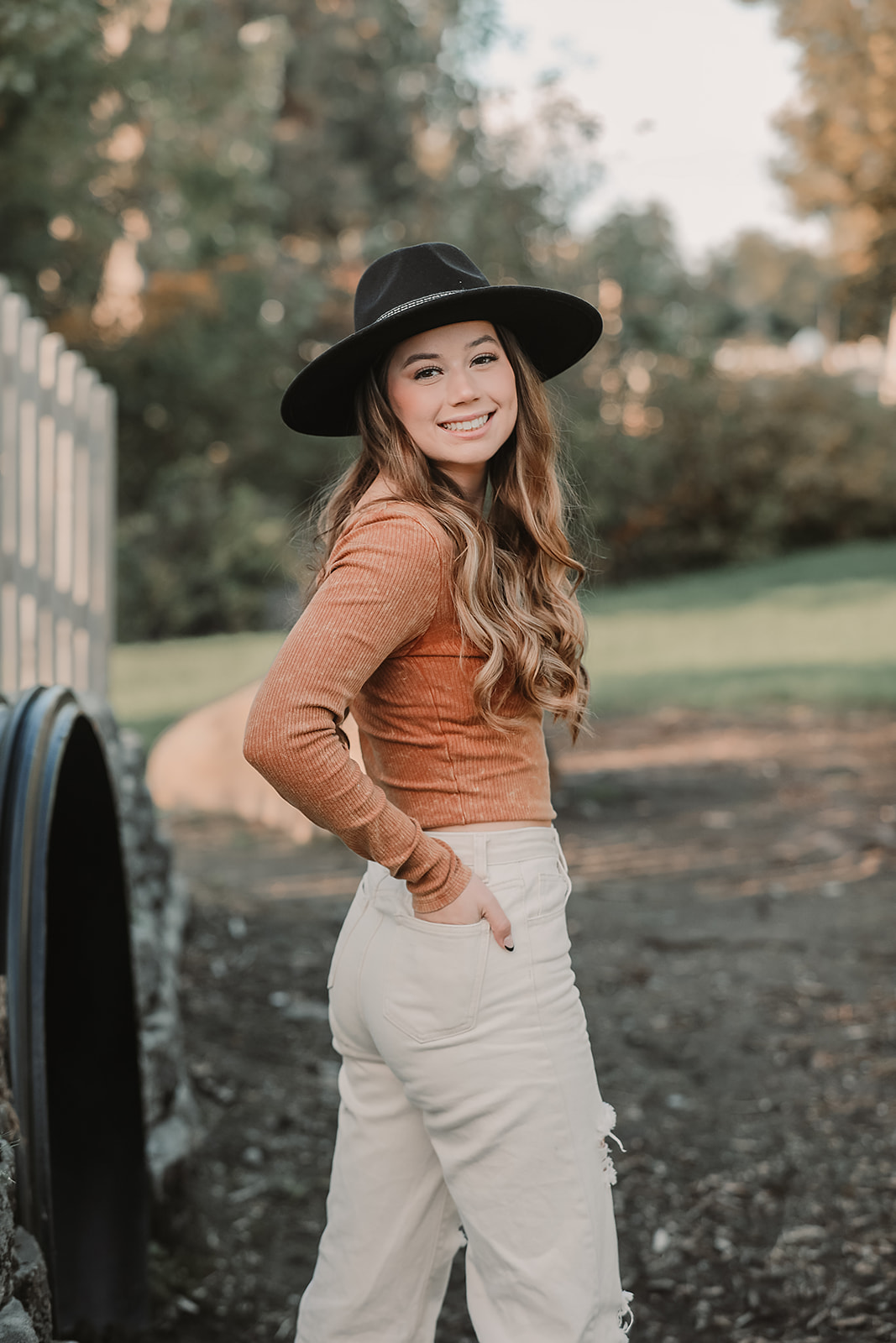 Senior in a black wide-brim hat and rust sweater on a garden path