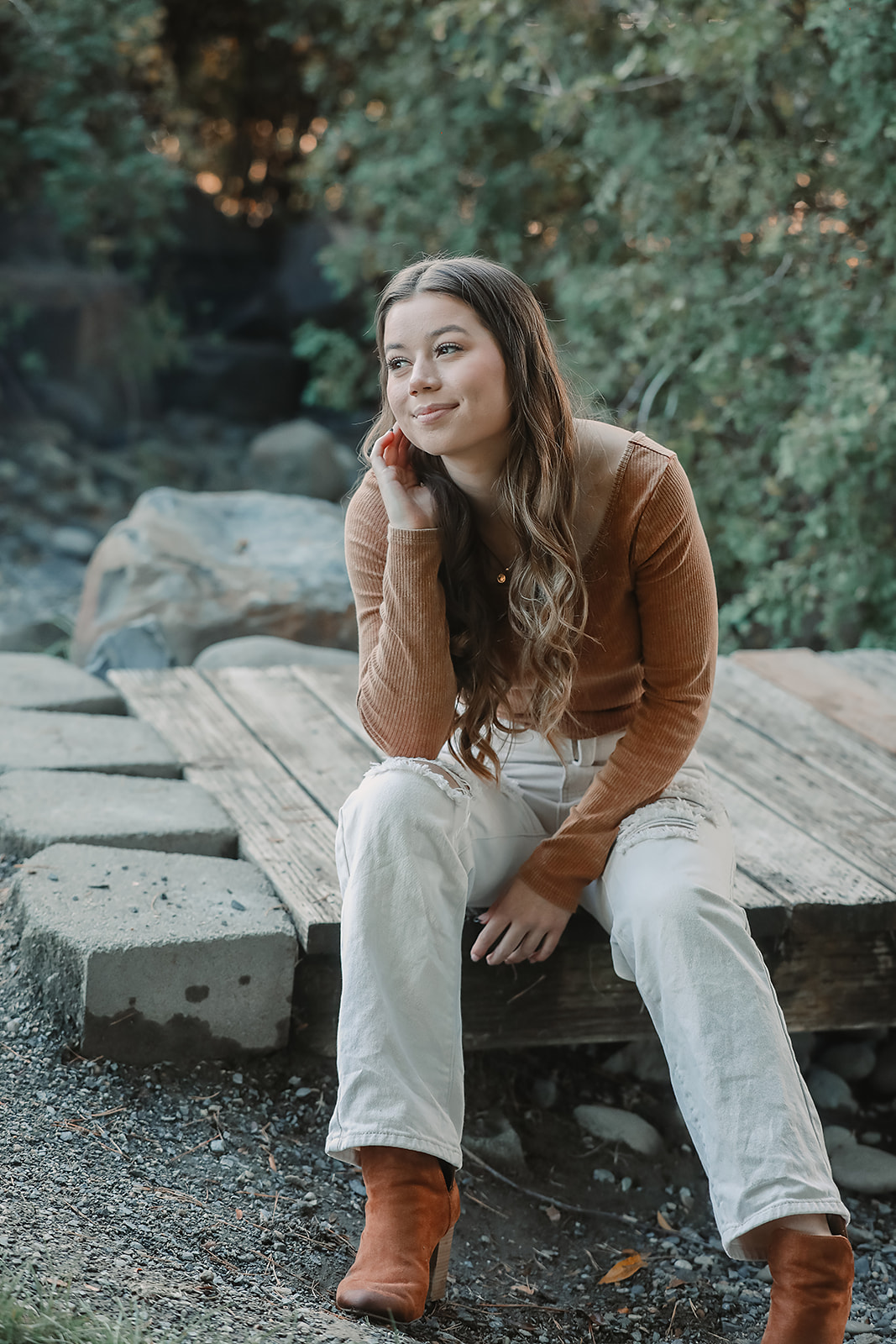 Senior seated on a wooden bridge in a rust sweater and tan boots